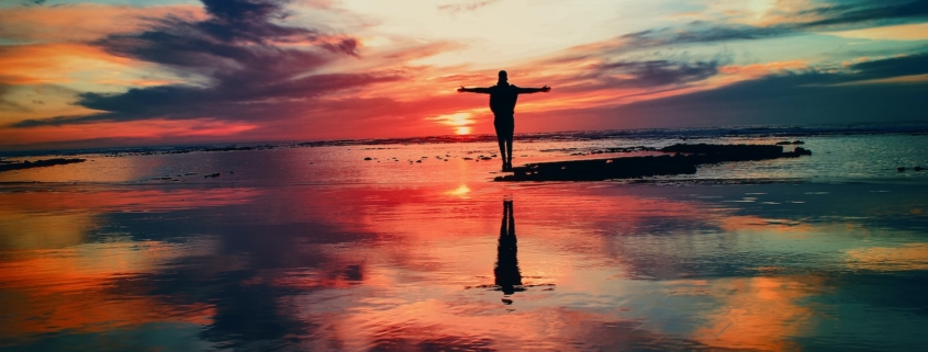 silhouette of person standing on rock surrounded by body of water